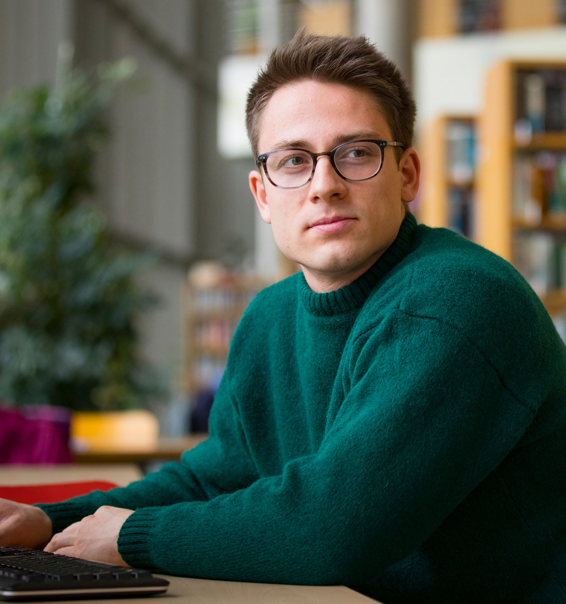 Man in glasses and a sweater sits at a desk.