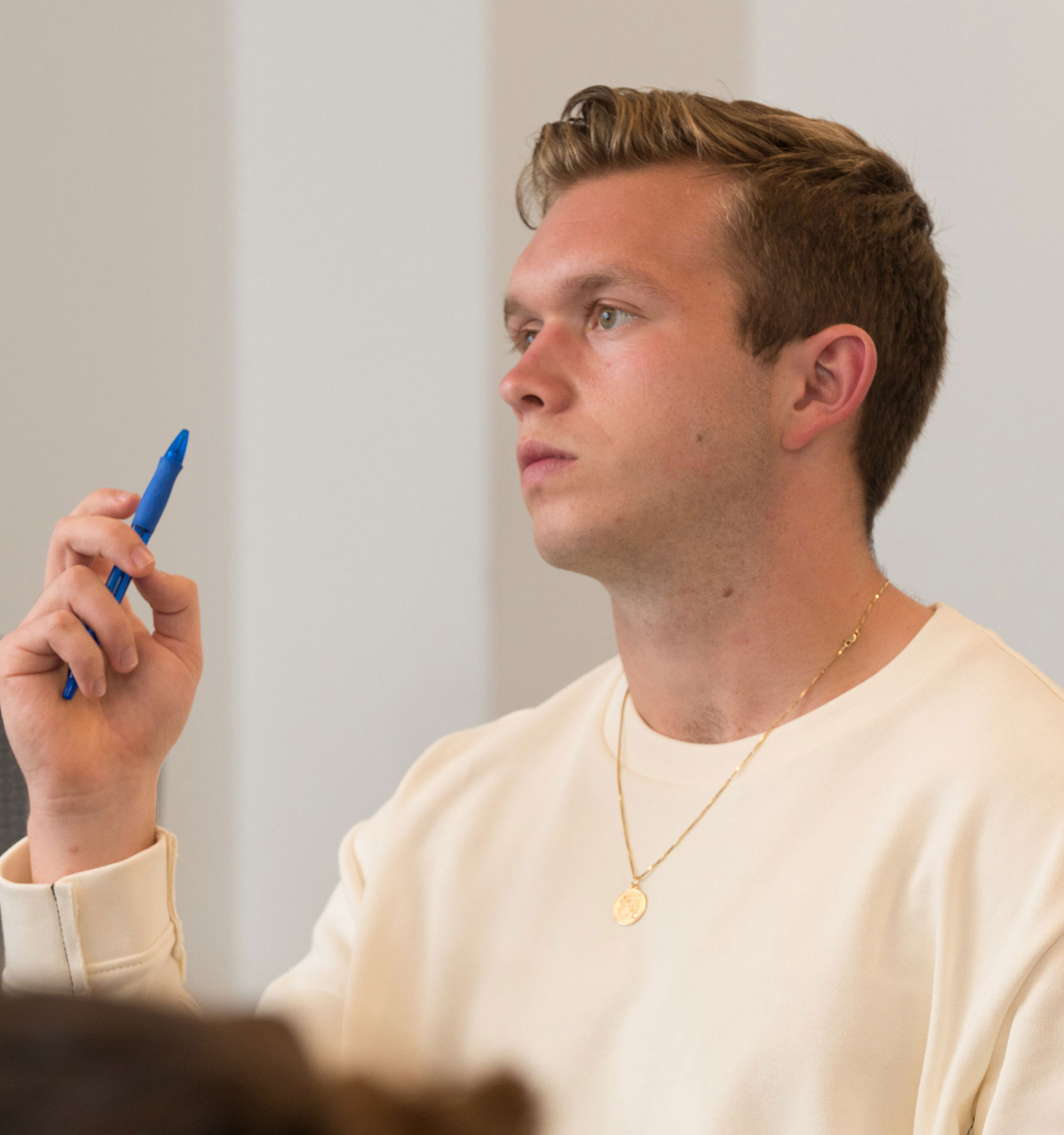 Student holds a pen and stares into the distance pensively.