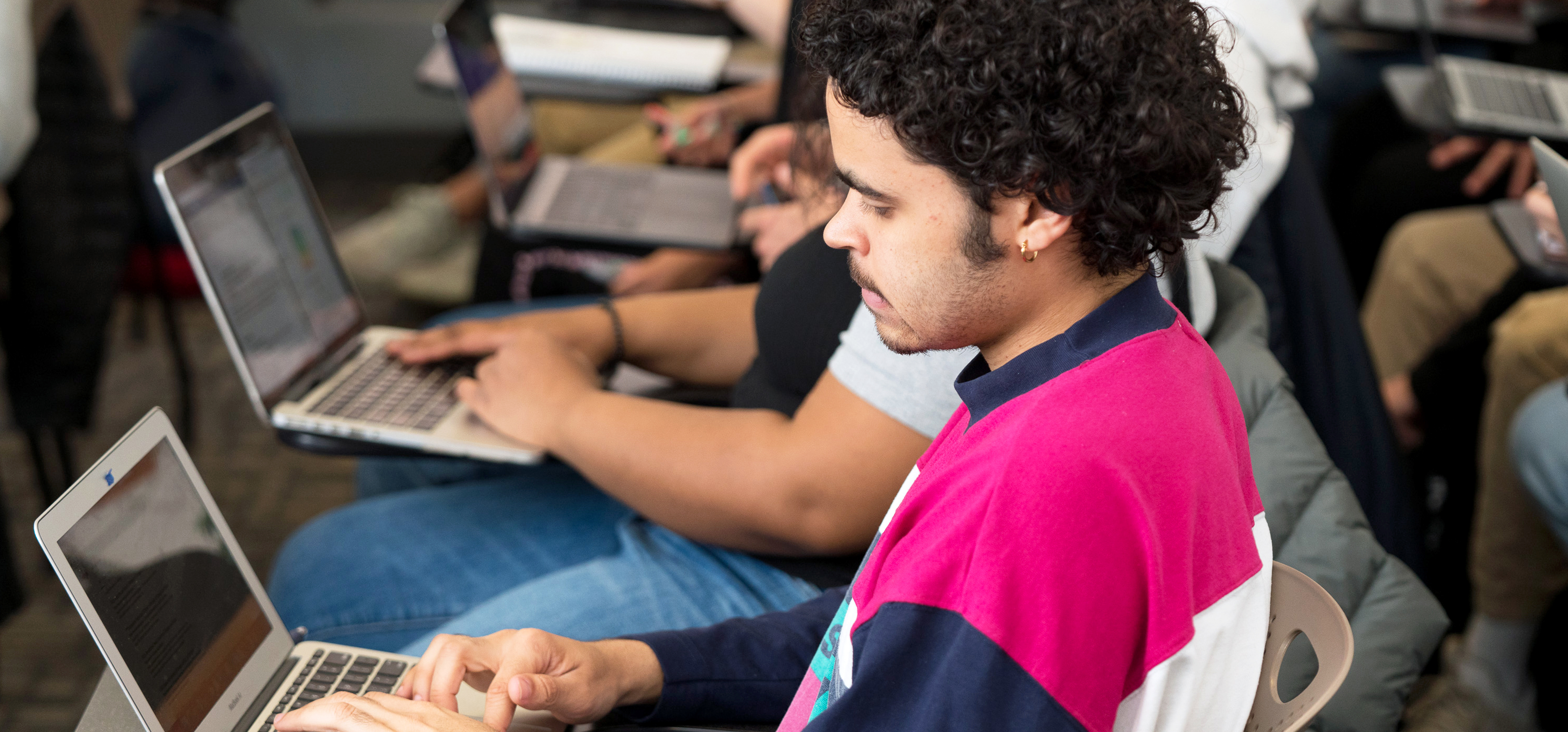 NYU SPS students sit in a row of desks while working on their laptops during a lecture