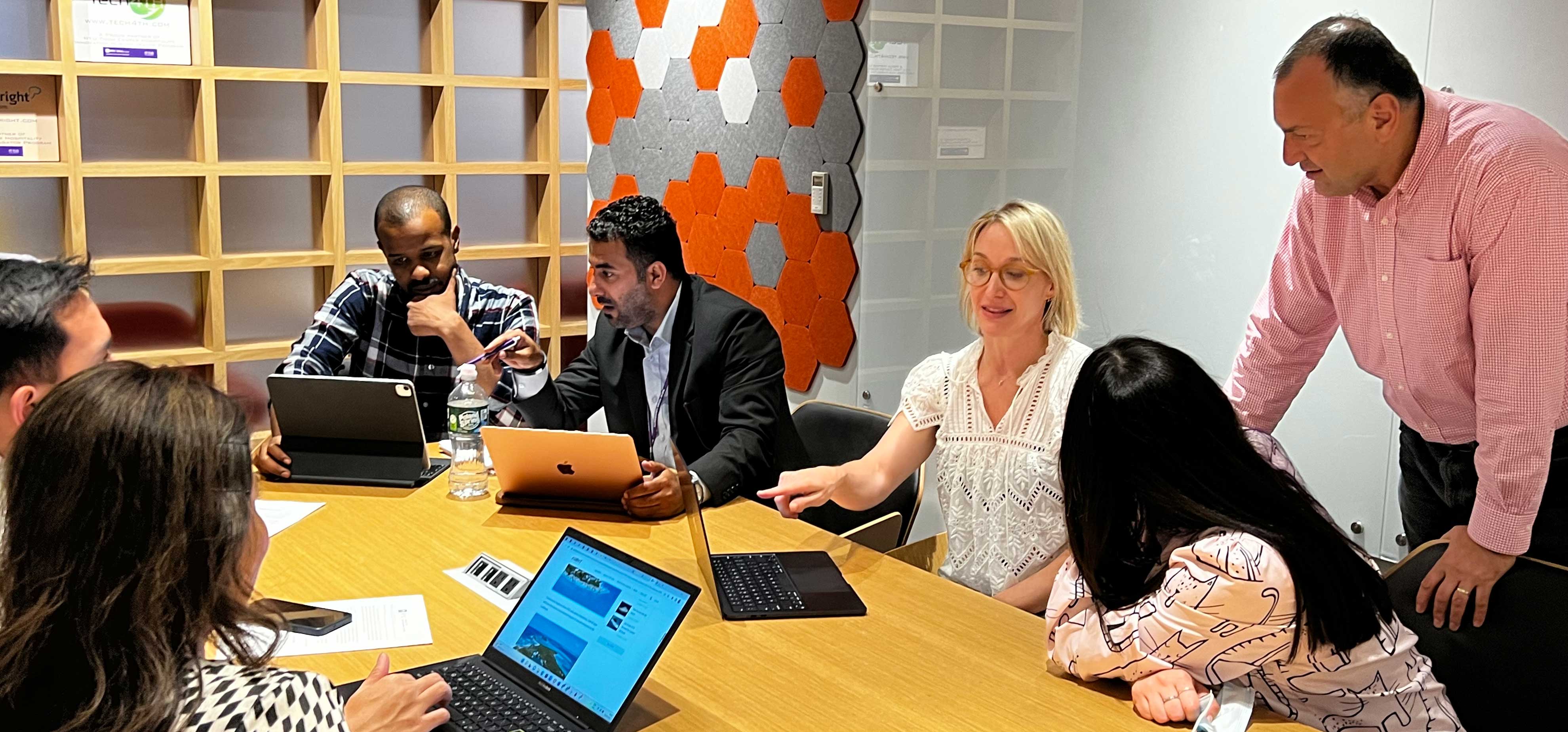 A group meeting in a modern office with laptops and geometric wall patterns.