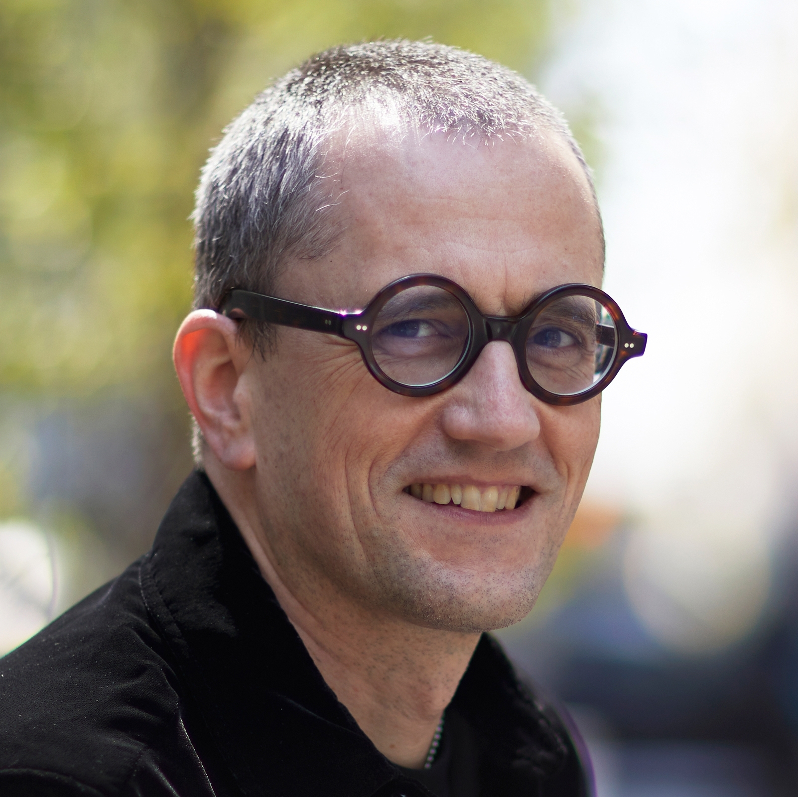 Pierre Gervois smiles for a headshot with a neutral outdoor background while wearing a black long sleeve shirt