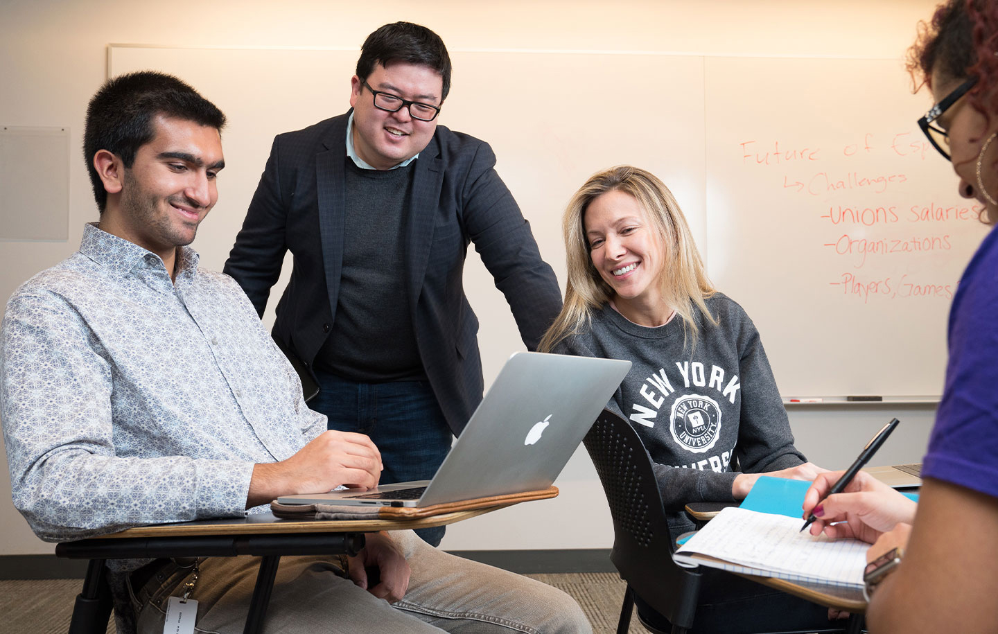 A group of NYU SPS students work on a project together while their professor looks at their work